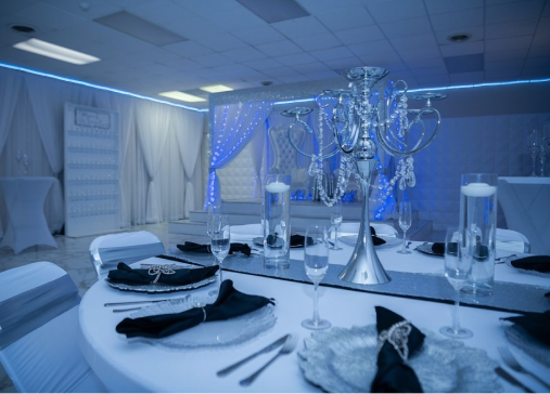 Elegant banquet table set for an event with blue lighting, featured prominently on the website's homepage. The setup includes crystal centerpieces, silver cutlery, and dark napkins on white tableclo