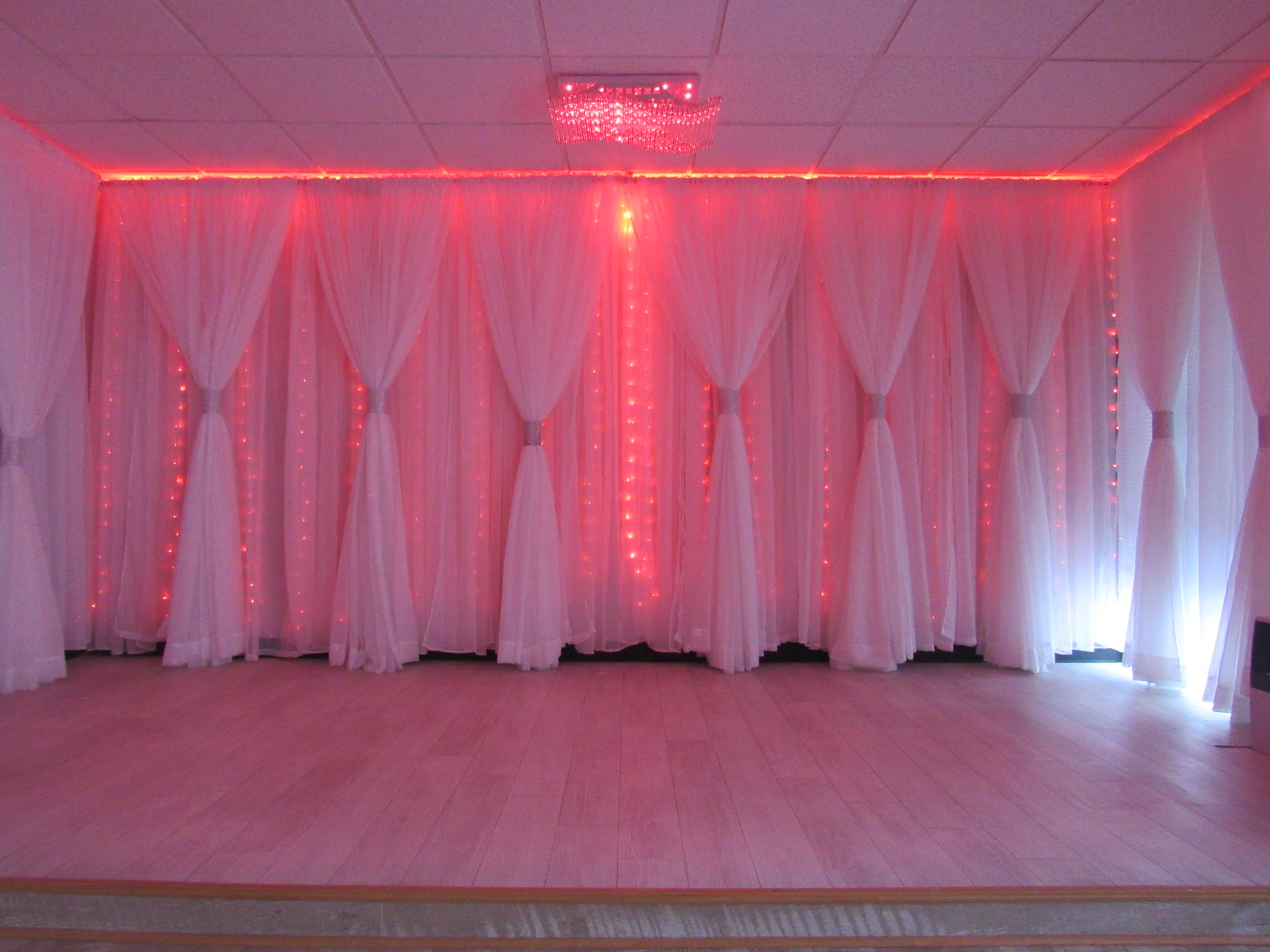 A dimly lit room in the Capitol Gallery with a row of white, sheer curtains along the wall, illuminated by pink lights, with a sparkling chandelier hanging from the ceiling.