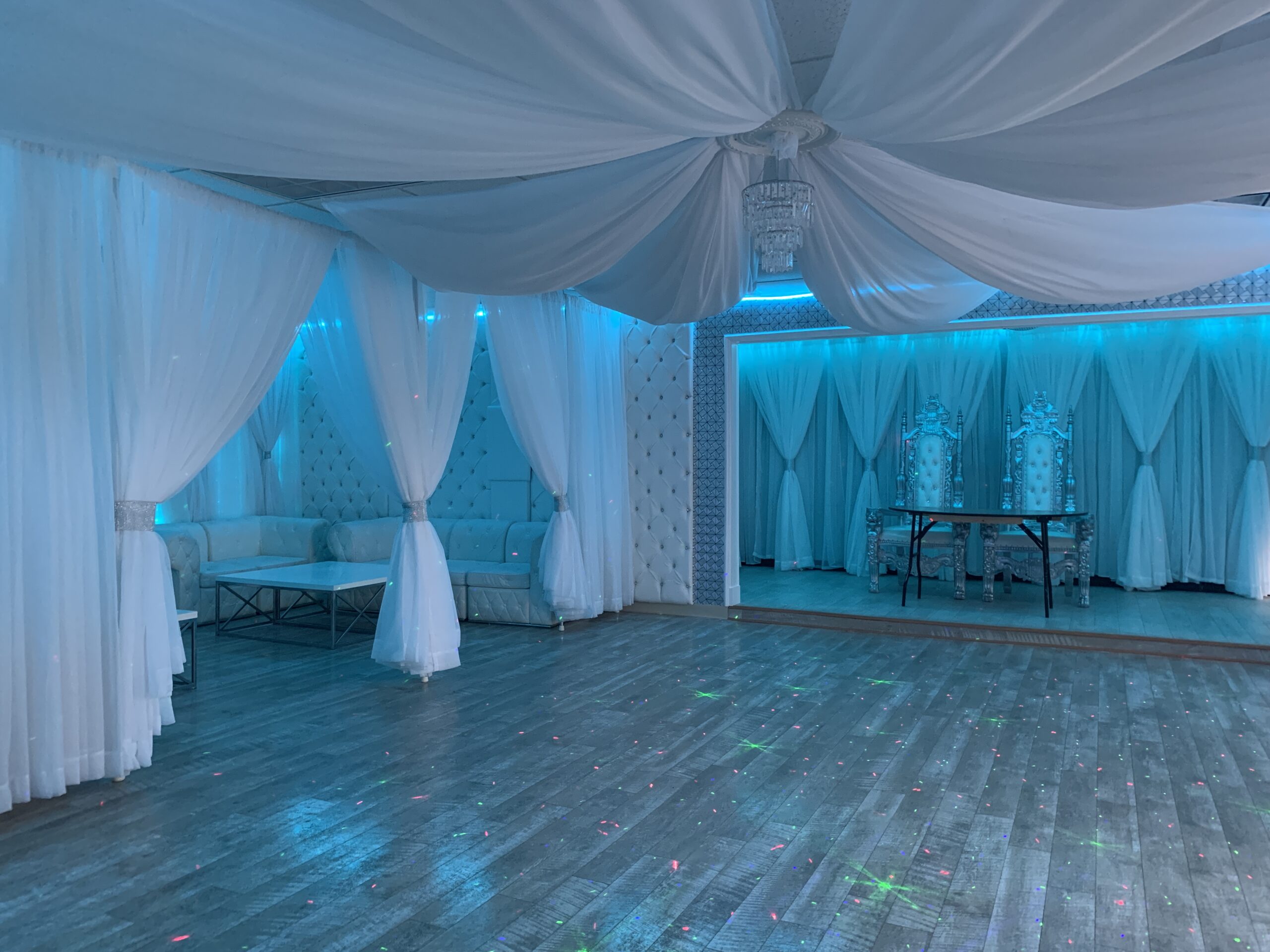 Elegant event hall decorated with white drapery, blue lighting, and an ornately carved white lounge area with sofas. A wooden dance floor in the Capitol Gallery reflects colorful lights.