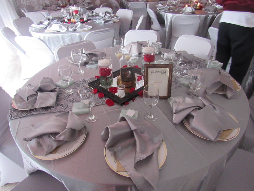 A well-arranged banquet table with grey tablecloths and napkins, elegant glassware, and plate settings, complemented by a central decorative piece with red candles at the Capitol Powerpack Gallery