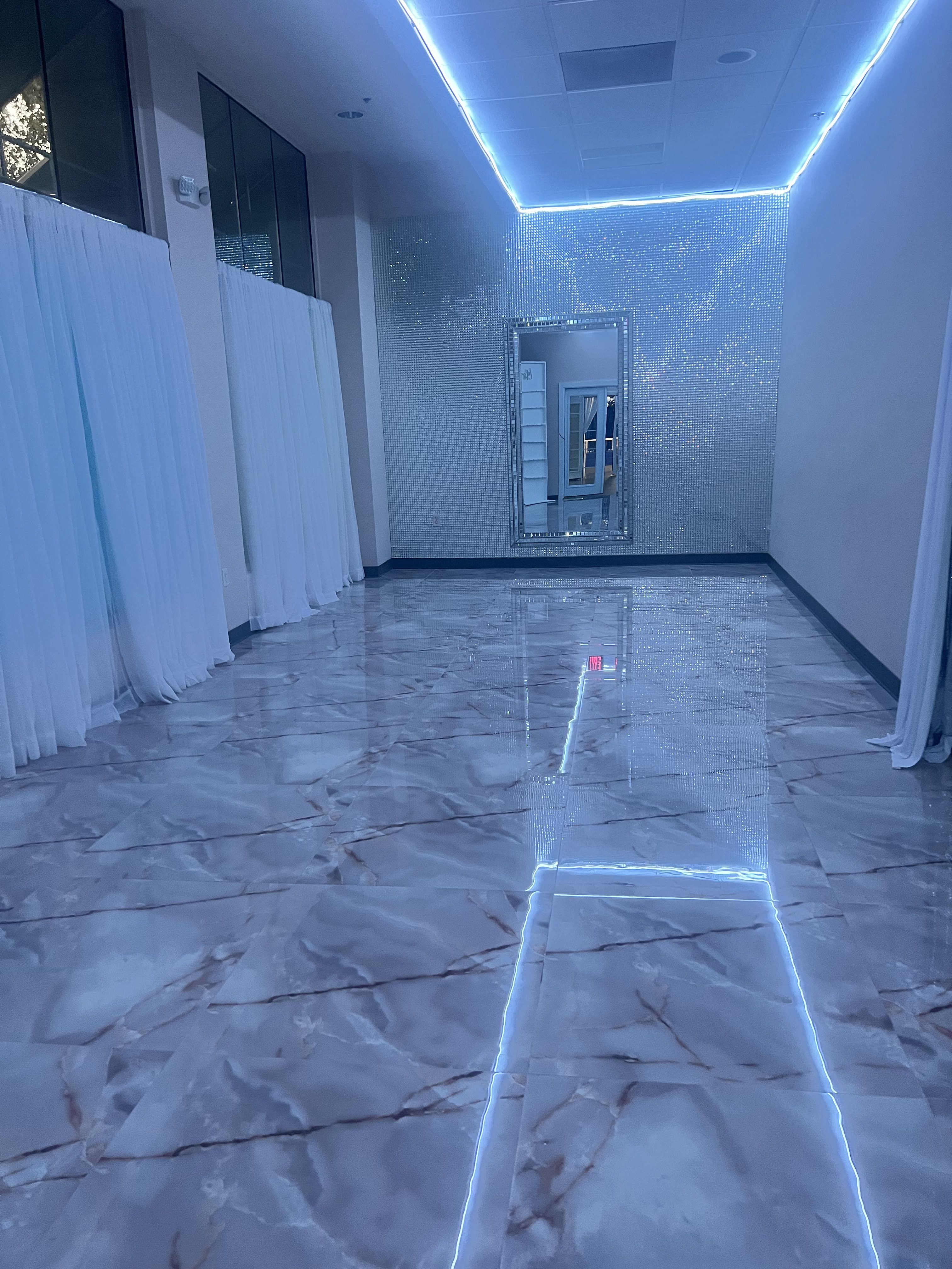 A narrow corridor illuminated by blue led lights along the edges and ceiling, with marble flooring and reflective walls, creating a futuristic ambiance.