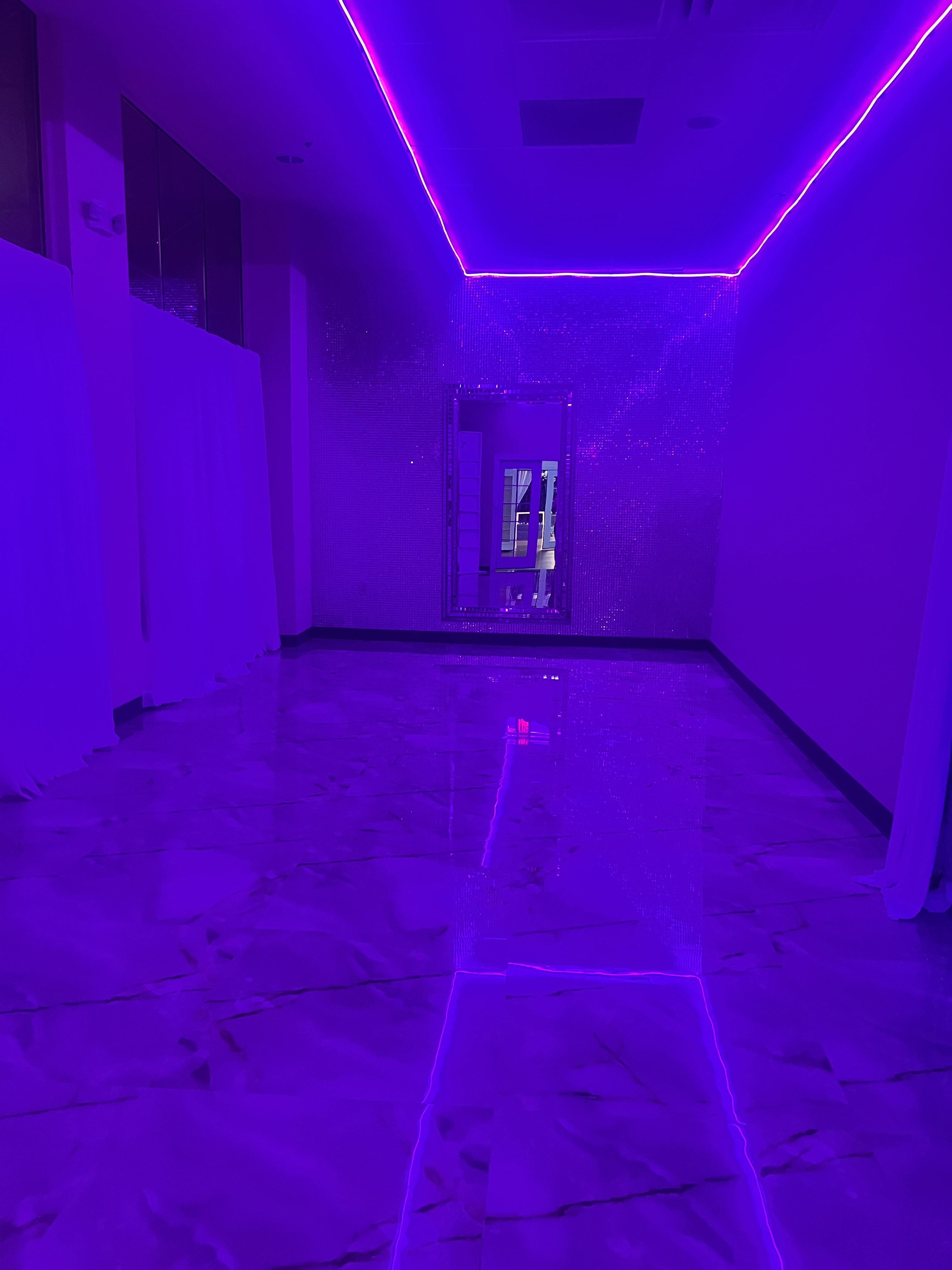A dimly lit corridor with a glossy marble floor, featuring pink and blue neon lights along the ceiling edges, reflecting on the surface to give a futuristic look.