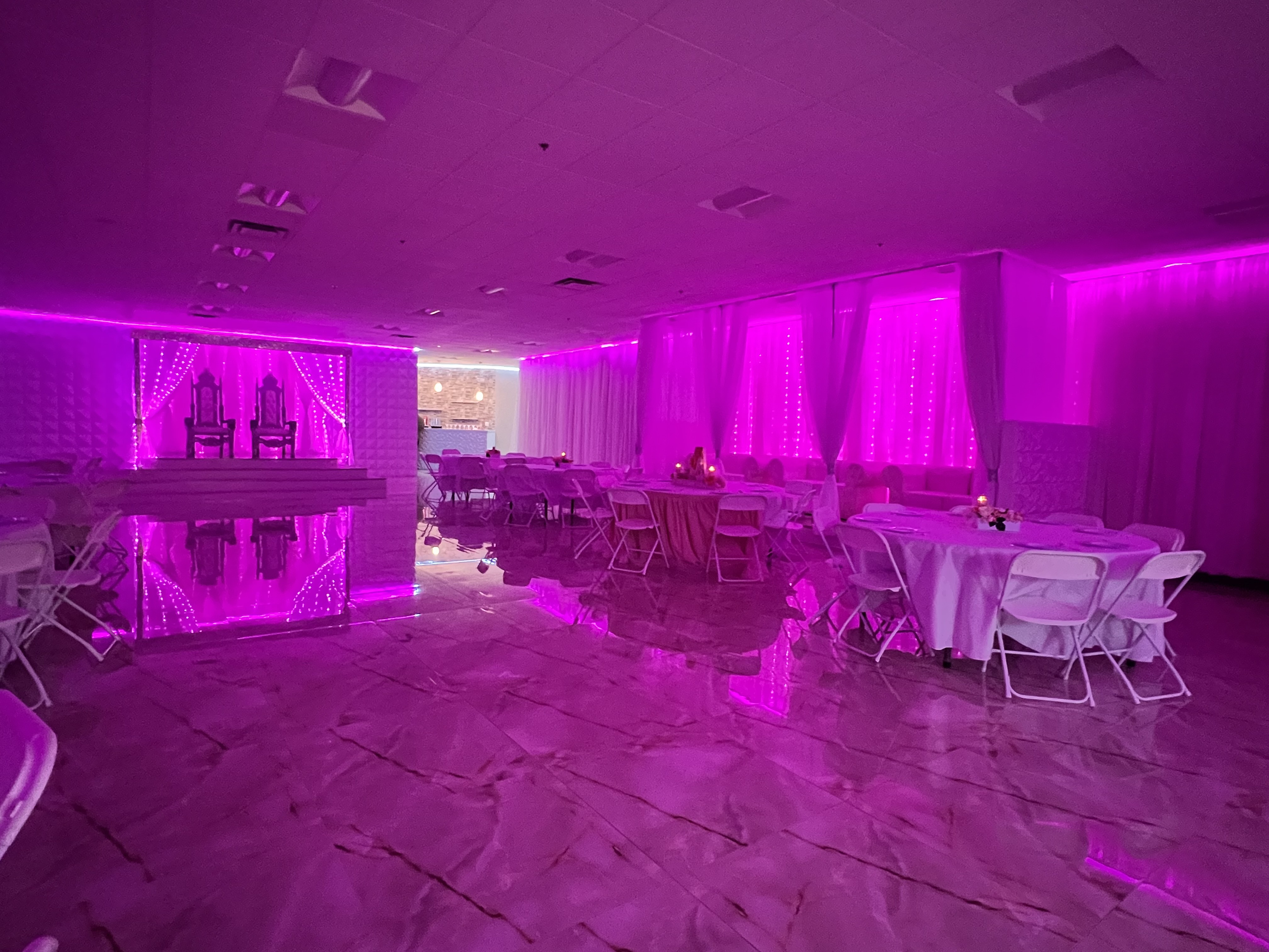 An event hall illuminated with purple lights, featuring set tables and reflective flooring under soft, ambient lighting.