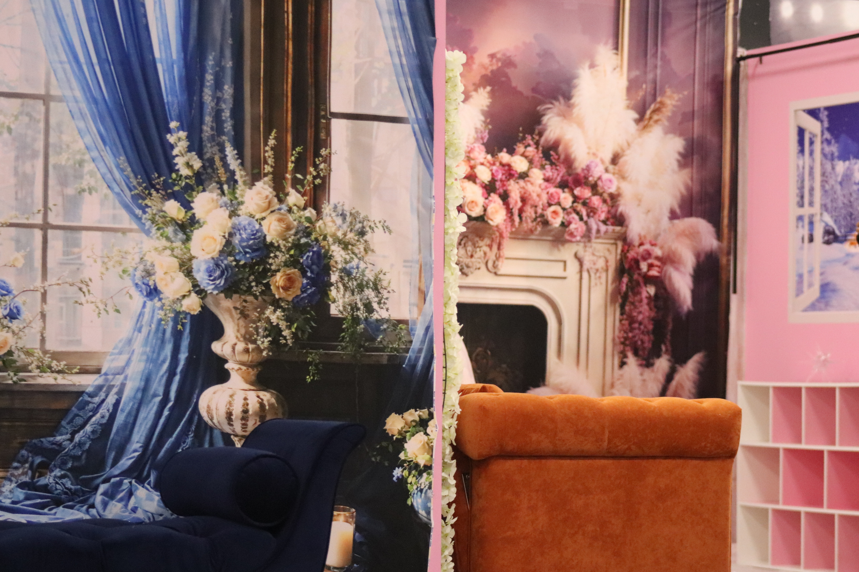 A cozy room corner featuring a dark blue draped bed with floral decorations beside a bright pink themed area with an ornate white fireplace and lush flowers.